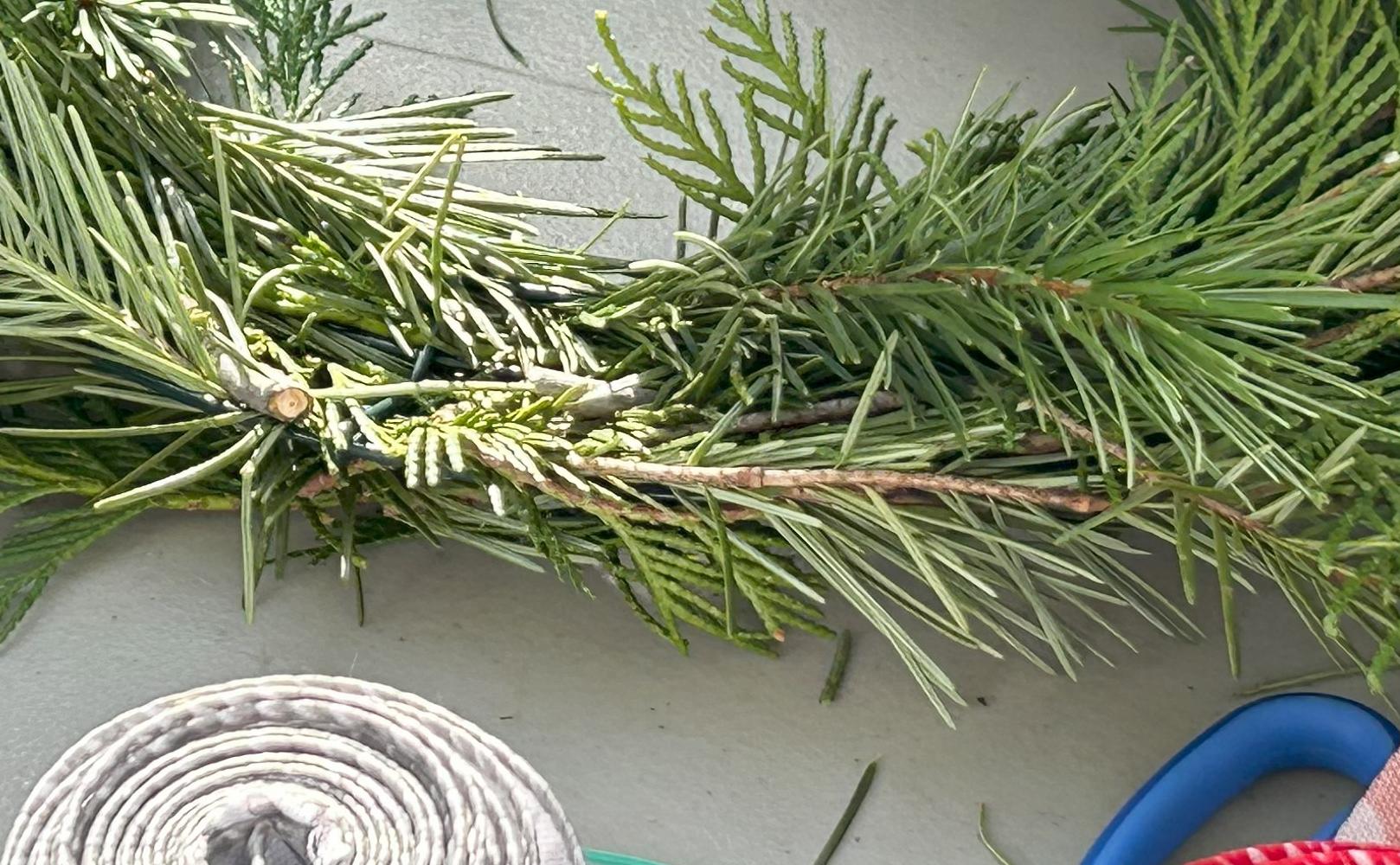 Human hands making a wreath out of pine fronds and wire.