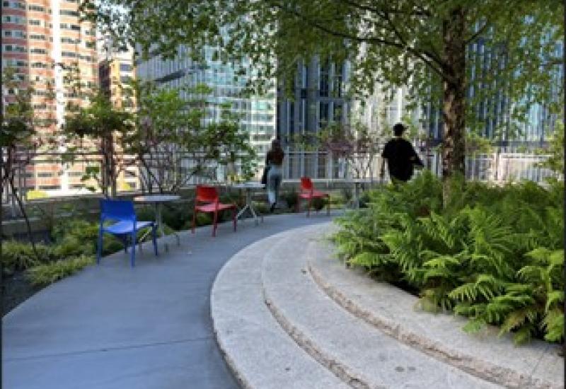 A curving pathway, surrounded by greenery and buildings in the background.